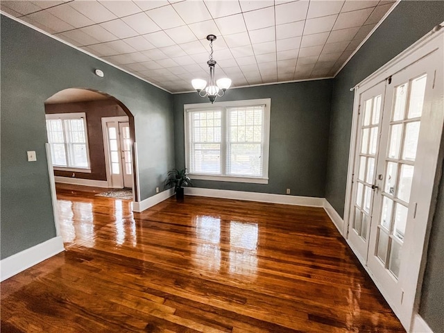 unfurnished dining area featuring an inviting chandelier, crown molding, french doors, and dark wood-type flooring