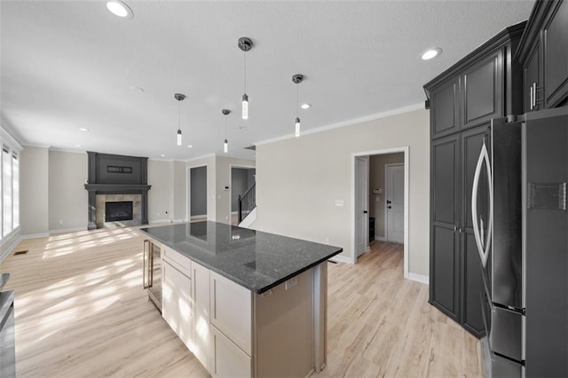 kitchen featuring light wood-type flooring, a fireplace, a kitchen island, stainless steel fridge, and crown molding