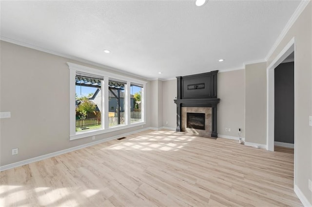 unfurnished living room featuring a tiled fireplace, ornamental molding, and light hardwood / wood-style flooring