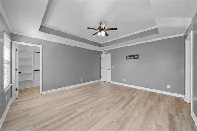 unfurnished bedroom featuring light hardwood / wood-style flooring, a spacious closet, a tray ceiling, and ceiling fan