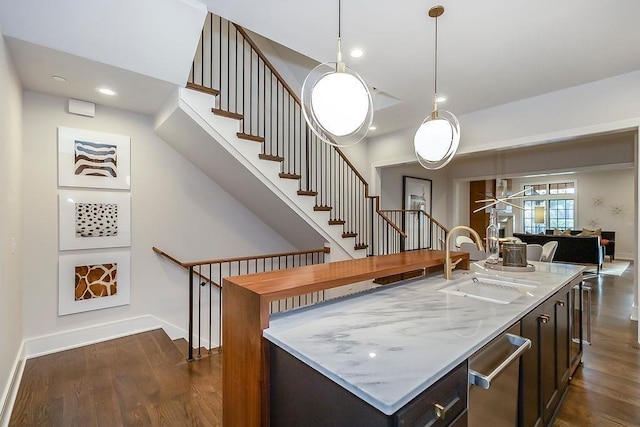 kitchen with light stone countertops, sink, decorative light fixtures, dark wood-type flooring, and a center island with sink