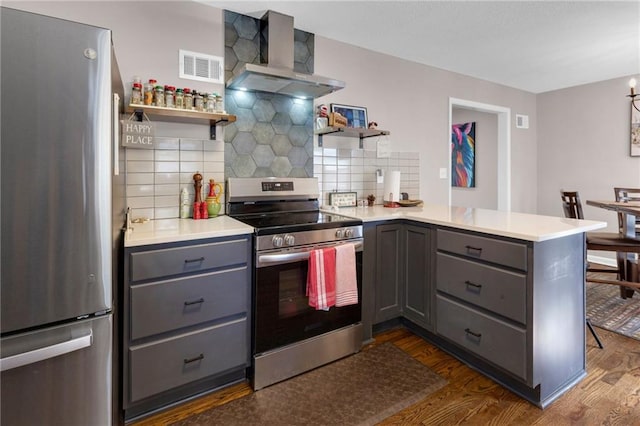 kitchen featuring wall chimney range hood, appliances with stainless steel finishes, dark hardwood / wood-style flooring, gray cabinets, and kitchen peninsula