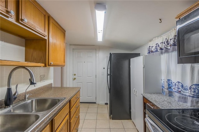 kitchen with decorative backsplash, range with electric cooktop, black refrigerator, sink, and light tile patterned floors