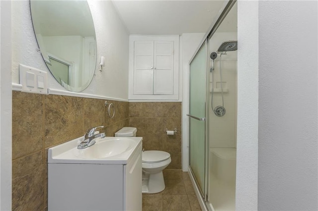 bathroom featuring a shower with door, toilet, tile patterned flooring, tile walls, and vanity