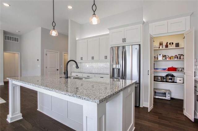 kitchen with a kitchen island with sink, sink, light stone countertops, pendant lighting, and white cabinets