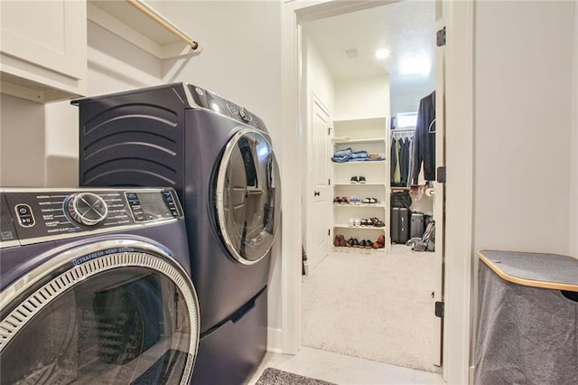 clothes washing area with washing machine and clothes dryer, light colored carpet, and cabinets