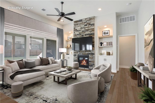 living room with built in shelves, hardwood / wood-style floors, a fireplace, and ceiling fan