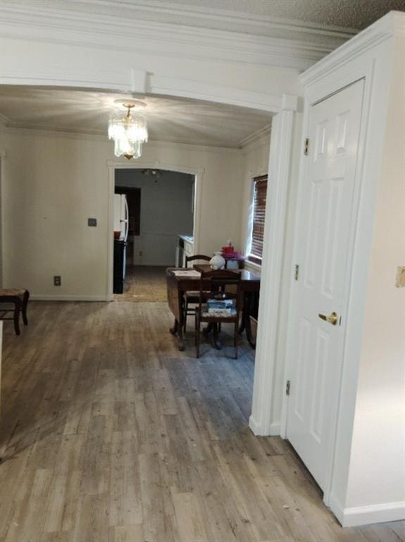 corridor with a notable chandelier, wood-type flooring, and ornamental molding