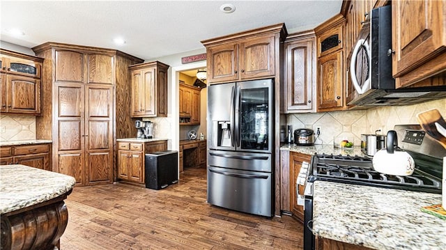 kitchen featuring stainless steel appliances, dark hardwood / wood-style floors, light stone countertops, and backsplash