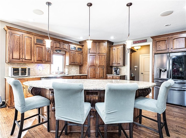 kitchen with stainless steel refrigerator with ice dispenser, a kitchen island, a breakfast bar area, and decorative light fixtures