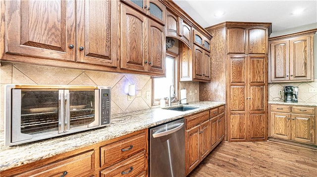 kitchen with sink, backsplash, stainless steel dishwasher, light stone countertops, and light wood-type flooring