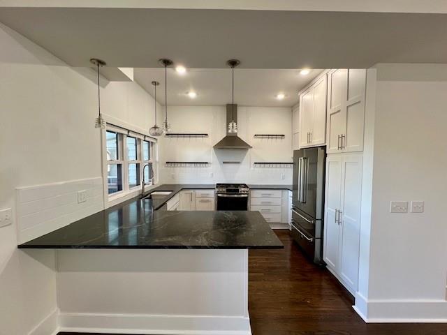 kitchen featuring sink, wall chimney range hood, kitchen peninsula, decorative light fixtures, and appliances with stainless steel finishes