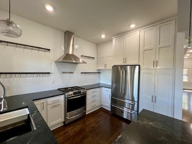 kitchen with wall chimney range hood, dark hardwood / wood-style floors, appliances with stainless steel finishes, decorative light fixtures, and white cabinetry