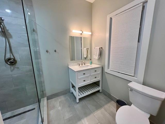 bathroom with tiled shower, vanity, and toilet