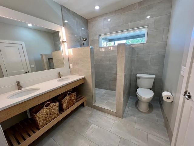 bathroom featuring vanity, tile patterned flooring, toilet, tiled shower, and tile walls