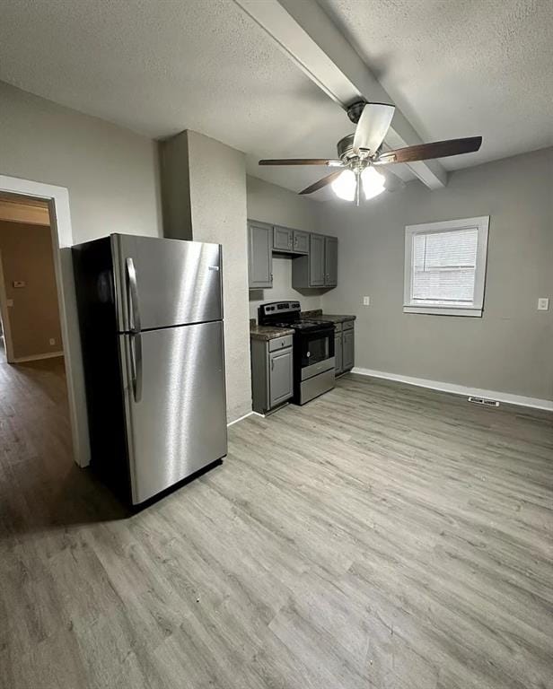 kitchen featuring beam ceiling, a textured ceiling, light wood-type flooring, gray cabinets, and stainless steel appliances