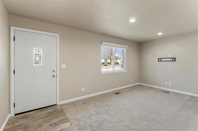 carpeted foyer featuring visible vents, recessed lighting, baseboards, and a textured ceiling