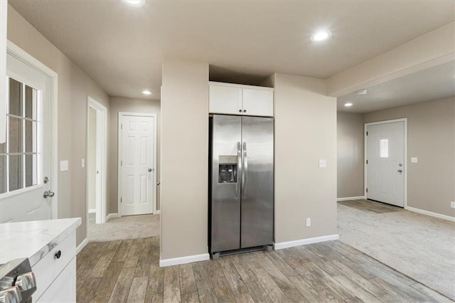 kitchen featuring baseboards, light wood-style flooring, light countertops, stainless steel refrigerator with ice dispenser, and white cabinetry