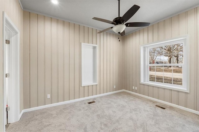 carpeted empty room featuring crown molding, a ceiling fan, visible vents, and baseboards