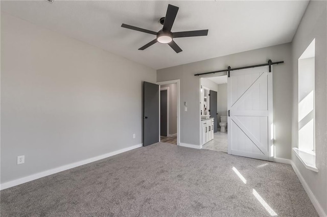 unfurnished bedroom featuring ensuite bathroom, a barn door, ceiling fan, and light colored carpet