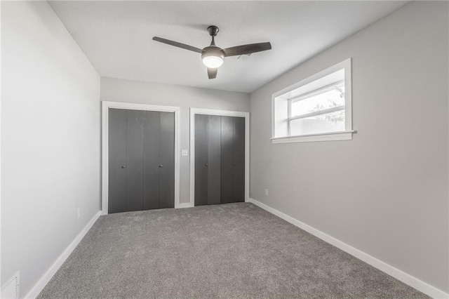 unfurnished bedroom featuring ceiling fan, multiple closets, and carpet