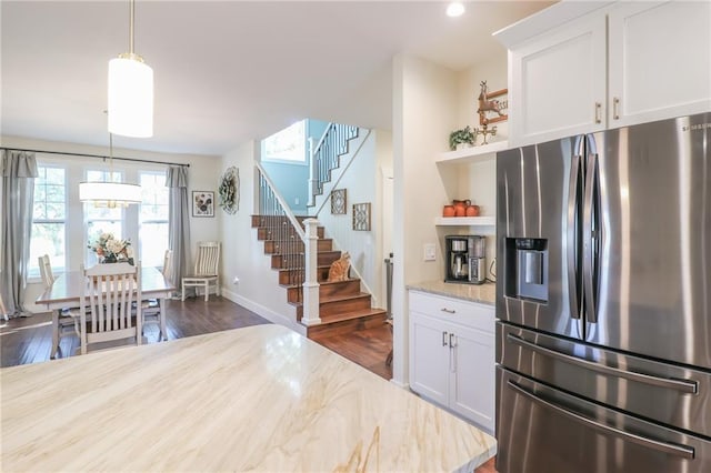 kitchen with stainless steel fridge, white cabinets, light stone countertops, and pendant lighting