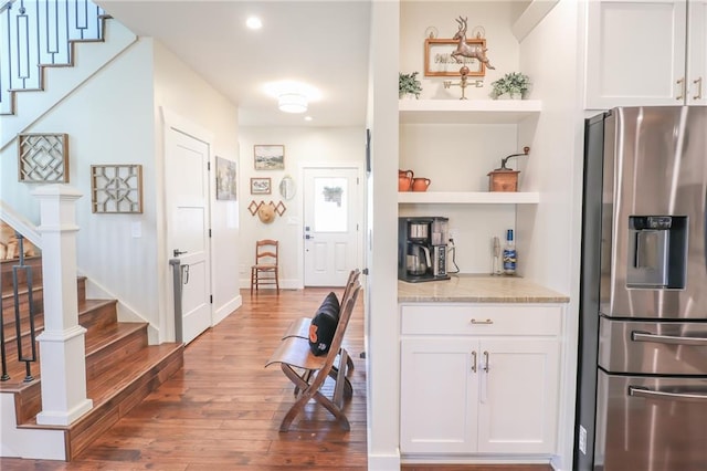 kitchen featuring white cabinetry, stainless steel refrigerator with ice dispenser, light stone countertops, and wood-type flooring