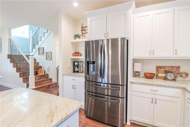 kitchen with light stone countertops, stainless steel refrigerator with ice dispenser, white cabinets, and hardwood / wood-style floors