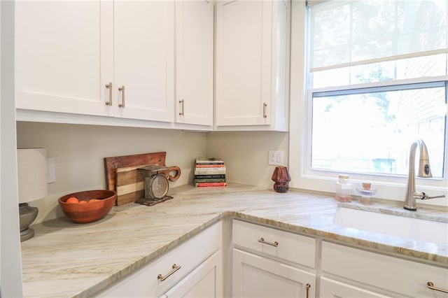 kitchen featuring white cabinets, light stone countertops, and sink