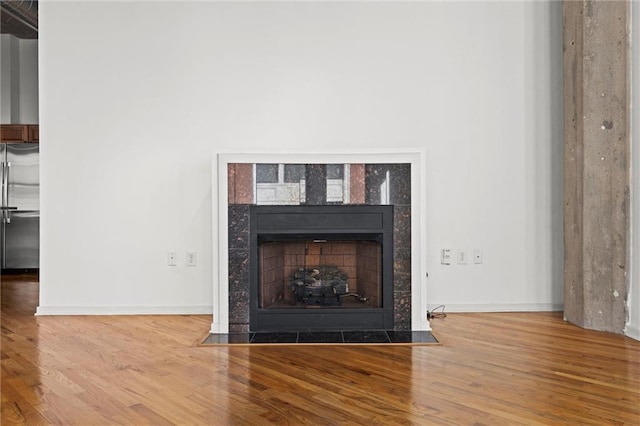 room details with hardwood / wood-style flooring, a tiled fireplace, and stainless steel refrigerator