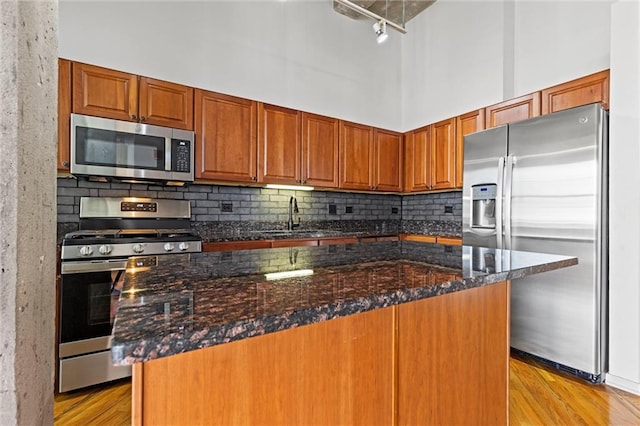 kitchen featuring sink, a kitchen island, light hardwood / wood-style floors, stainless steel appliances, and dark stone counters