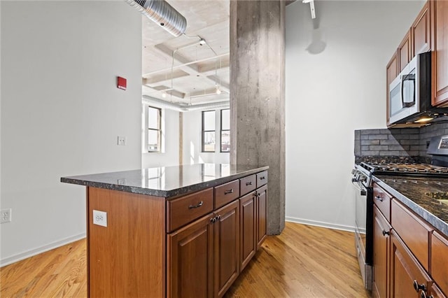 kitchen with decorative backsplash, a kitchen island, light hardwood / wood-style flooring, dark stone counters, and appliances with stainless steel finishes