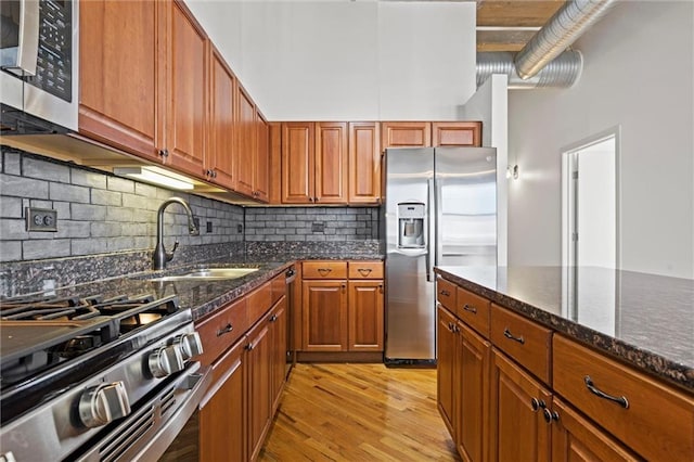 kitchen featuring tasteful backsplash, appliances with stainless steel finishes, sink, light wood-type flooring, and dark stone countertops