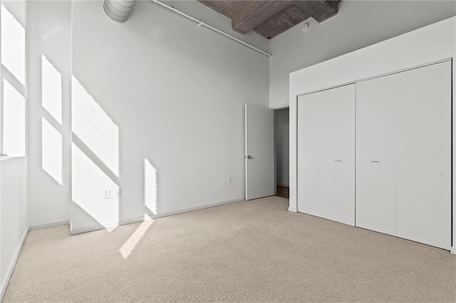 unfurnished bedroom with light carpet, a closet, beam ceiling, and a high ceiling