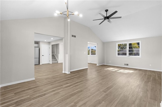 unfurnished living room featuring hardwood / wood-style flooring, high vaulted ceiling, ceiling fan with notable chandelier, and plenty of natural light