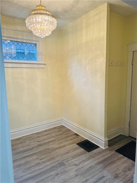 empty room with a textured ceiling, wood-type flooring, and an inviting chandelier