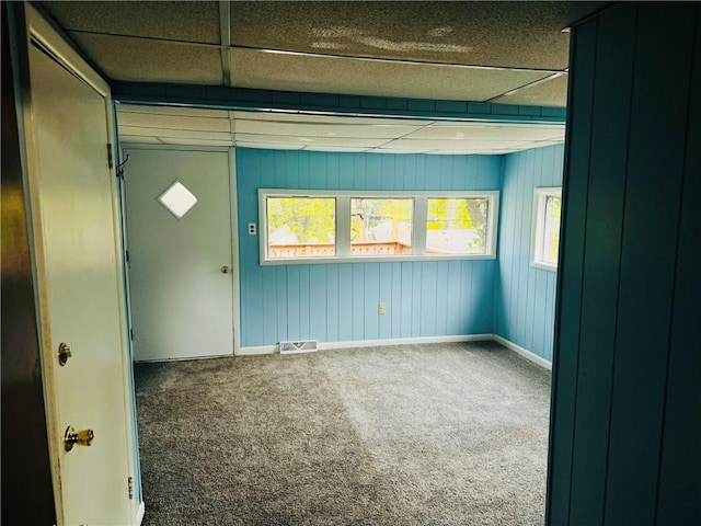 carpeted empty room with wood walls and a paneled ceiling