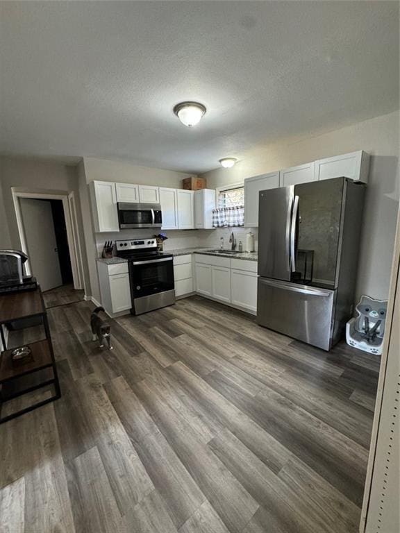 kitchen featuring white cabinets, appliances with stainless steel finishes, a textured ceiling, hardwood / wood-style flooring, and sink