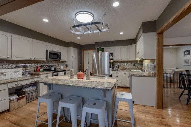320 Jones Ave, Warrensburg, MO 64093 - kitchen featuring appliances with stainless steel finishes, a kitchen bar, backsplash, light wood-type flooring, and a textured ceiling