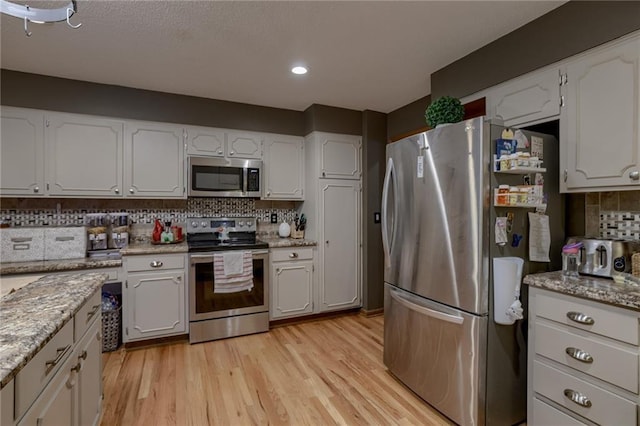 kitchen featuring decorative backsplash, white cabinetry, stainless steel appliances, and light hardwood / wood-style floors