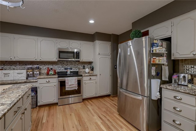 320 Jones Ave, Warrensburg, MO 64093 - kitchen with appliances with stainless steel finishes, decorative backsplash, light wood-style flooring, white cabinets, and light stone countertops