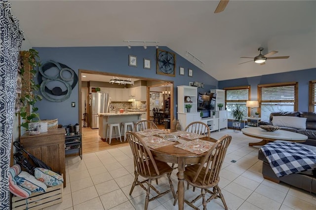 tiled dining room with high vaulted ceiling, ceiling fan with notable chandelier, and rail lighting