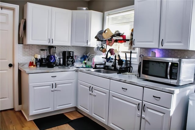 kitchen with white cabinetry, sink, light wood-type flooring, and backsplash