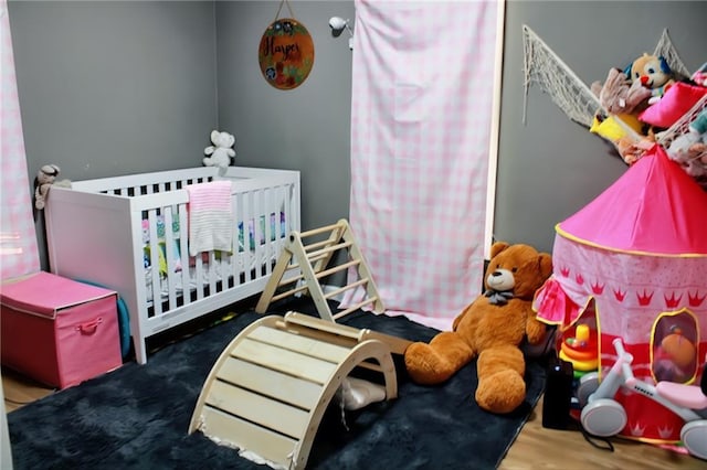 bedroom with wood-type flooring and a nursery area