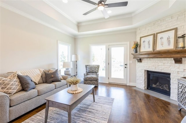 living room featuring dark hardwood / wood-style floors, a tray ceiling, crown molding, a fireplace, and ceiling fan