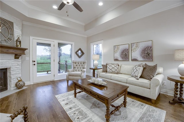 living room with a fireplace, ceiling fan, wood finished floors, and a tray ceiling