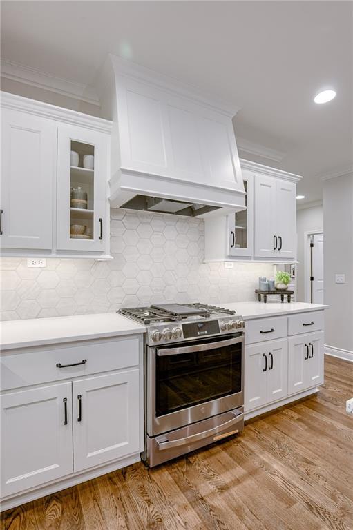 kitchen featuring white cabinetry, crown molding, light countertops, stainless steel range with gas stovetop, and custom exhaust hood