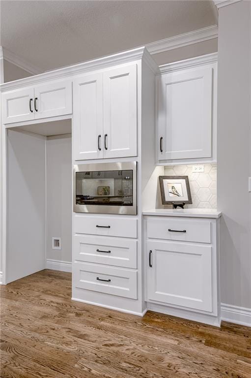 interior space with built in microwave, wood finished floors, backsplash, and ornamental molding