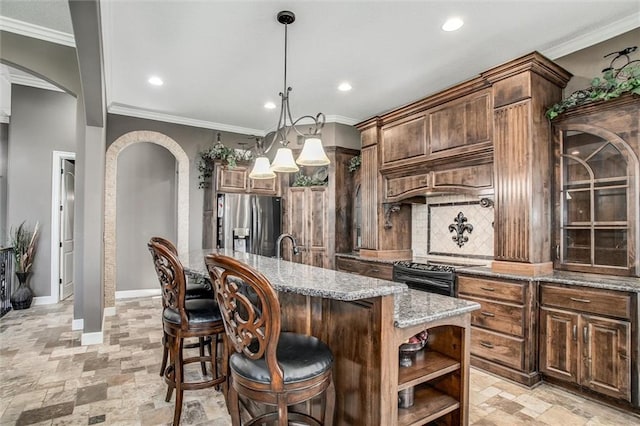 kitchen with light stone counters, a kitchen island with sink, black range, stainless steel fridge with ice dispenser, and hanging light fixtures