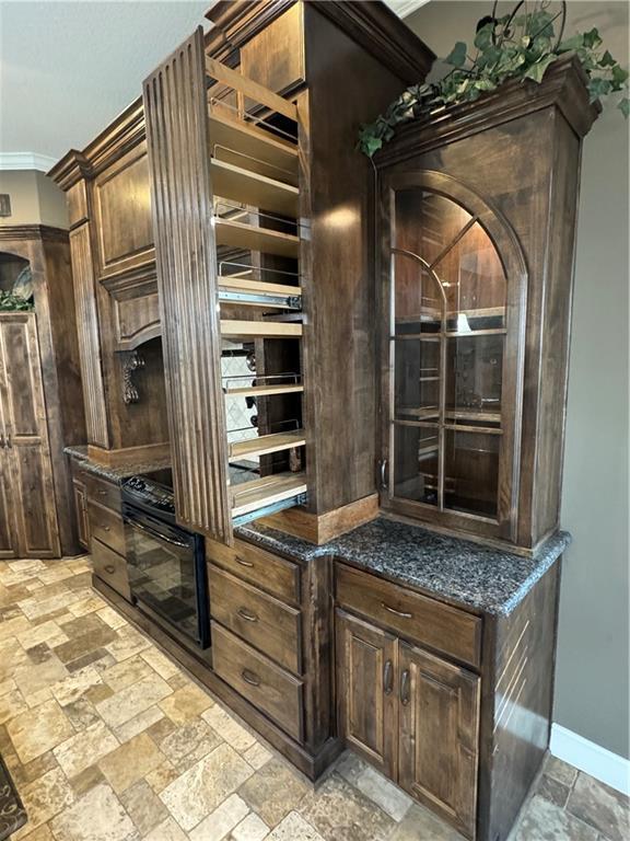 kitchen featuring dark brown cabinetry, dark stone counters, and ornamental molding